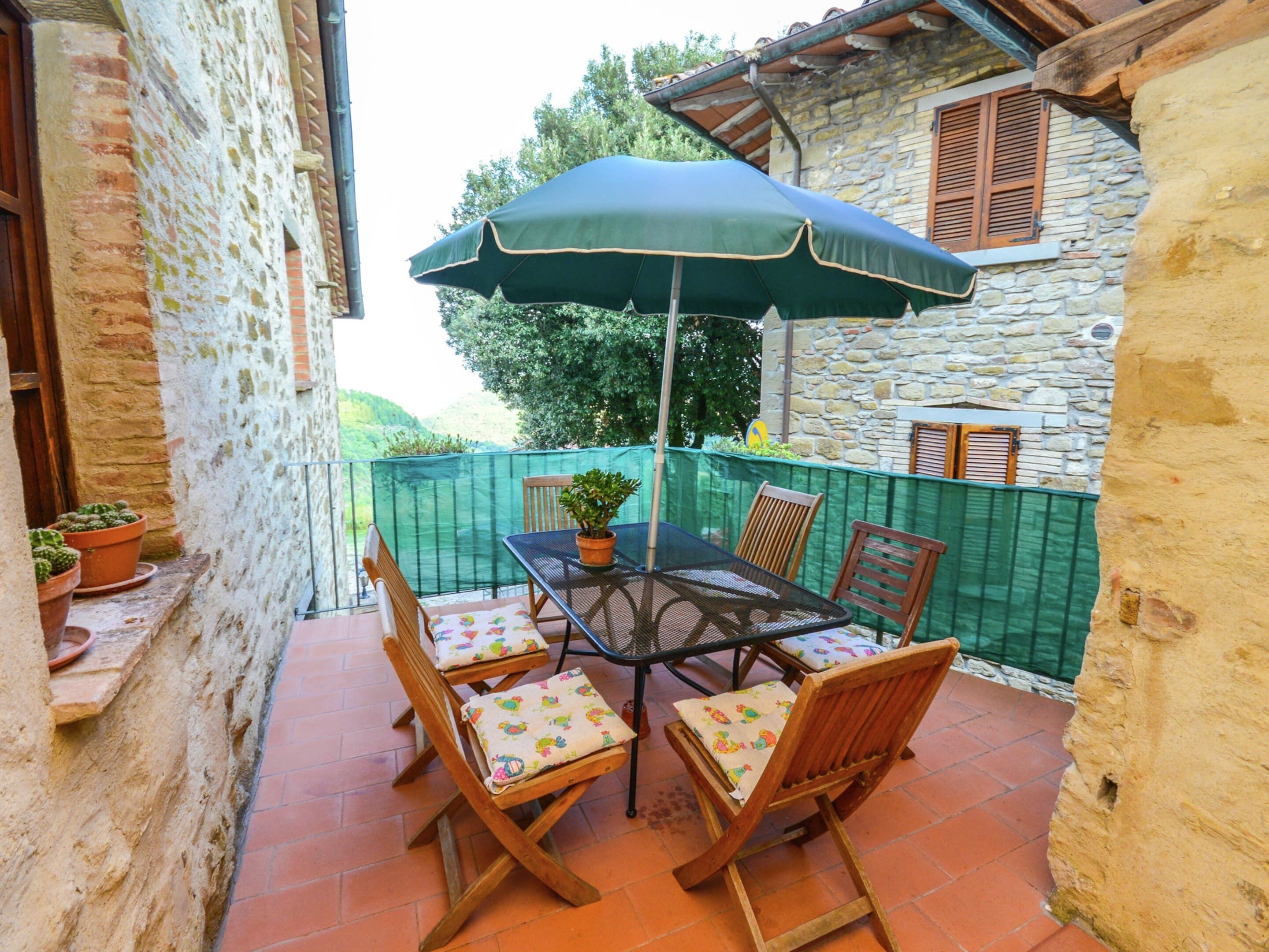 Une terrasse avec une table et des chaises, un parasol vert et des plantes en pot.
