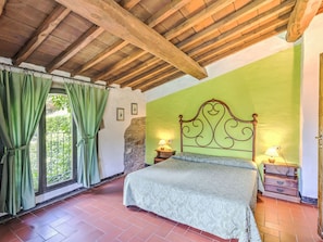 Un dormitorio con cama, cortinas verdes, pared de piedra y techo de madera.