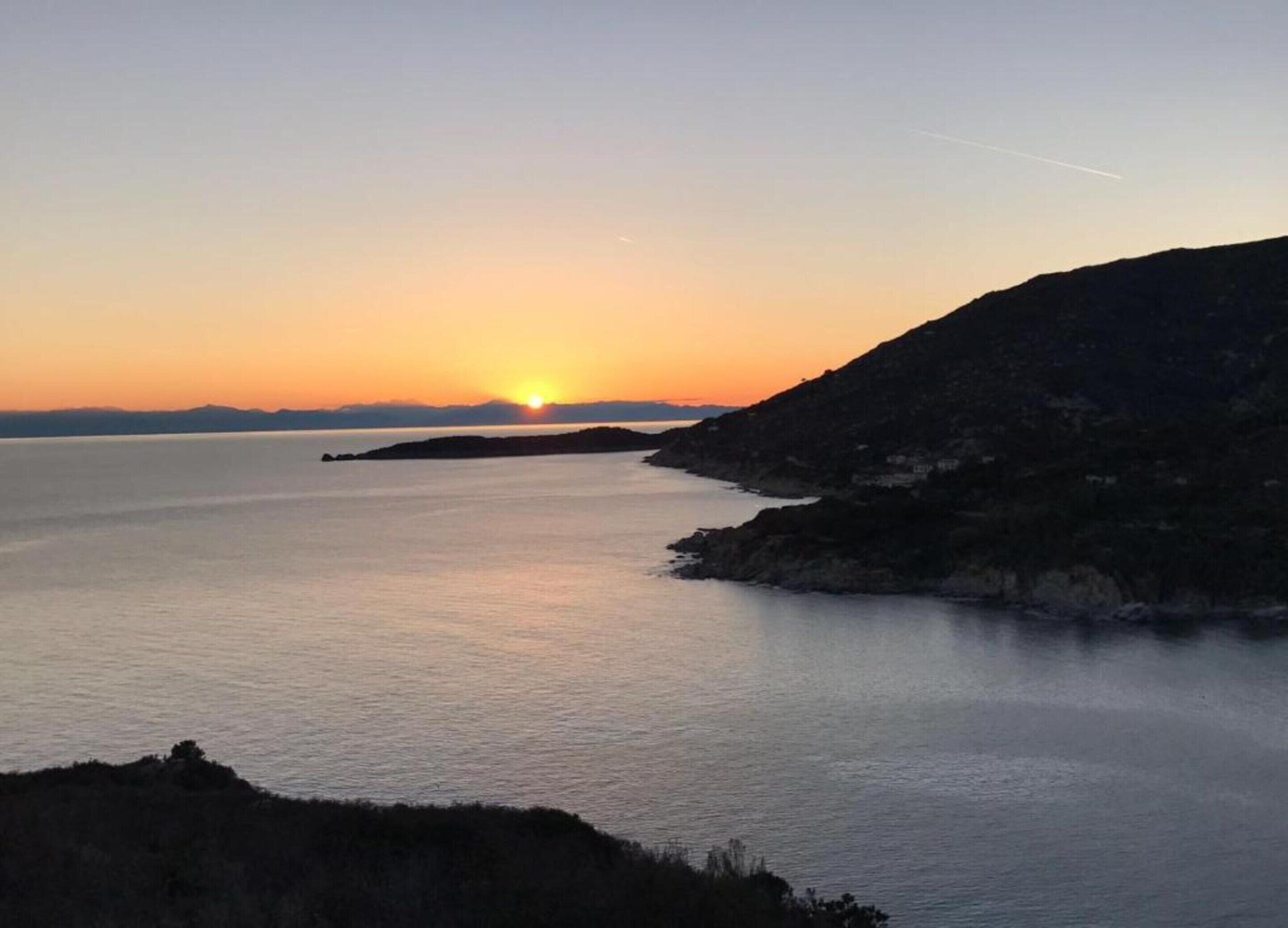 A coastal sunset view with calm waters and distant landforms.