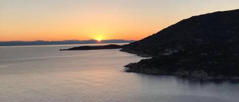 A coastal sunset view with calm waters and distant landforms.