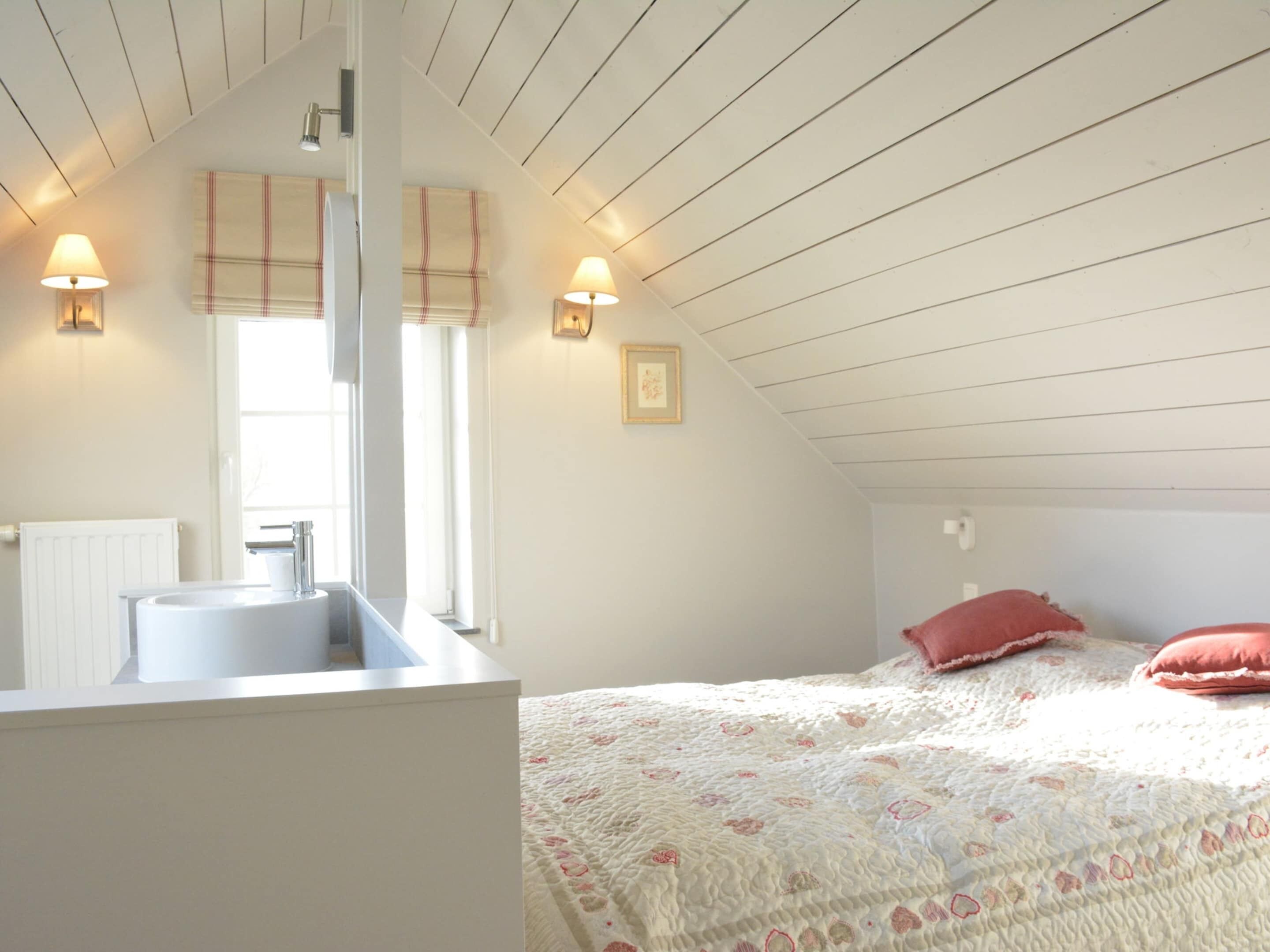 A bedroom with a white bed, a bedside table, a window with blinds, and a white radiator.