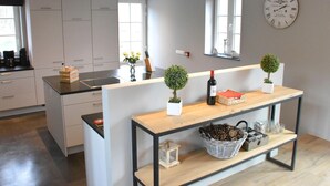 A modern kitchen with white cabinets, a wooden island, and a wall clock. - Peaceful Forest Stay in Gesves (Gesves)