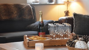 A cozy living room with a wooden coffee table, a bottle of champagne, glasses, snacks, and decorative pinecones. - Peaceful Forest Stay in Gesves (Gesves)