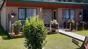 A small brick house with a green roof, two windows with white curtains, and a small porch with a bench. - Cozy Apartment in Boltenhagen Germany near Beach (Boltenhagen)