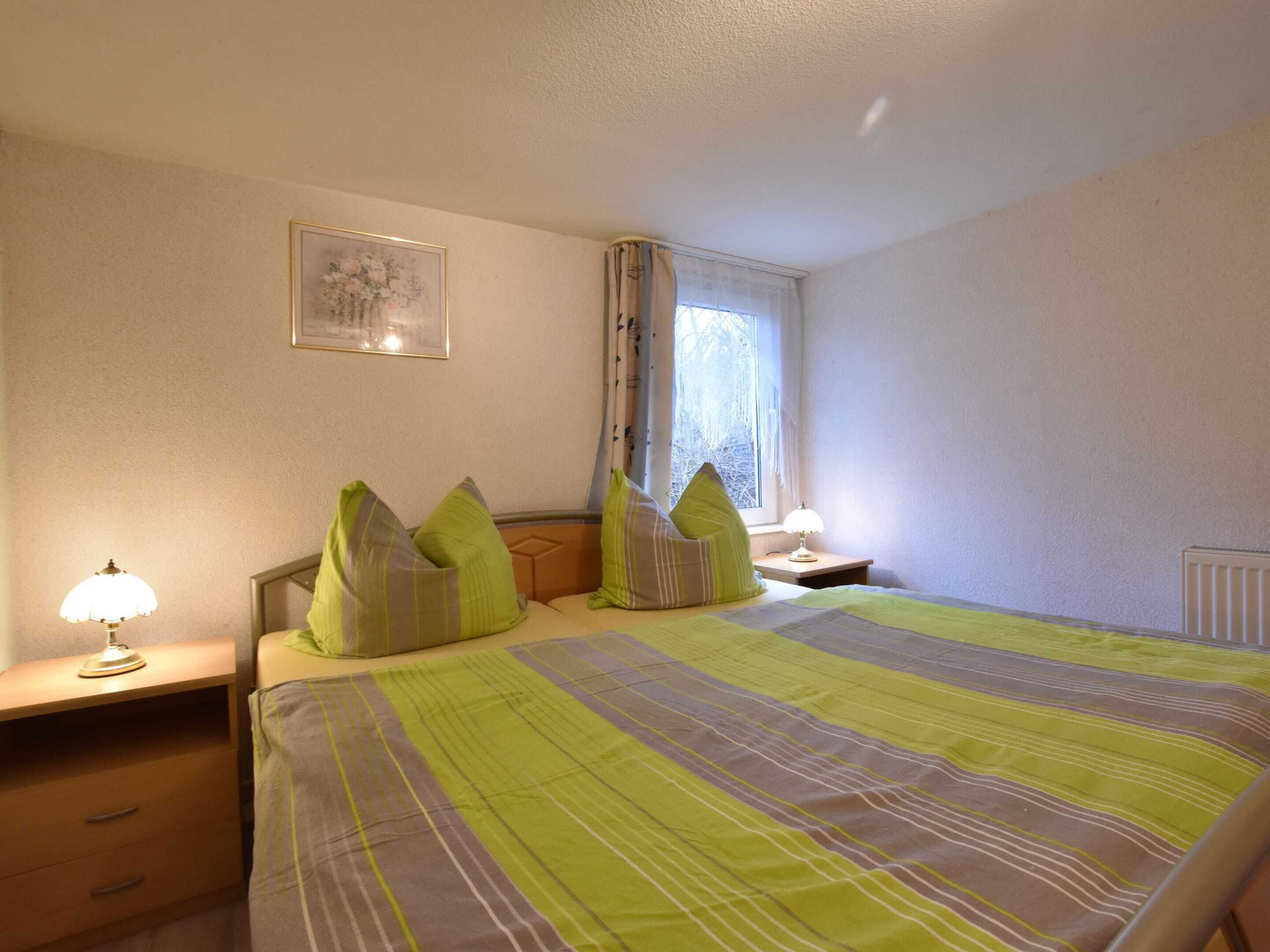 A bedroom with a bed, two bedside tables, a lamp, a window with curtains, and a framed picture on the wall.