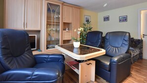 A living room with a dining table, two blue leather chairs, a cabinet with glass doors, and a potted plant. - Cozy Apartment in Boltenhagen Germany near Beach (Boltenhagen)