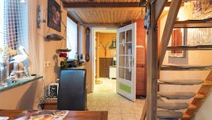 A rustic interior with a wooden staircase, a dining area with a table and chairs, and a kitchen area with a stove and various kitchen items. - Charmante Ferienwohnung in Wismar mit Garten (Wismar)
