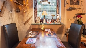A rustic dining area with a wooden table, two chairs, a hanging light fixture, and a window with blinds. - Charmante Ferienwohnung in Wismar mit Garten (Wismar)