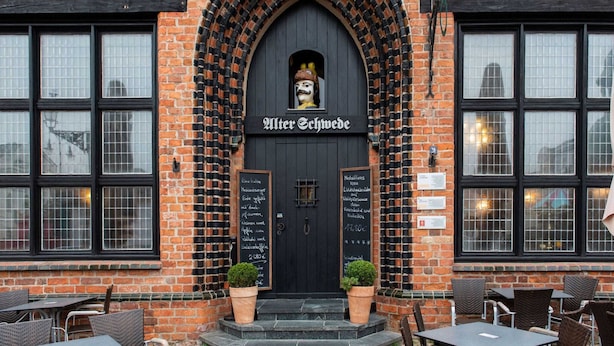A brick building with a black arched entrance, two windows on either side, and outdoor seating with chairs and tables. - Charmante Ferienwohnung in Wismar mit Garten (Wismar)