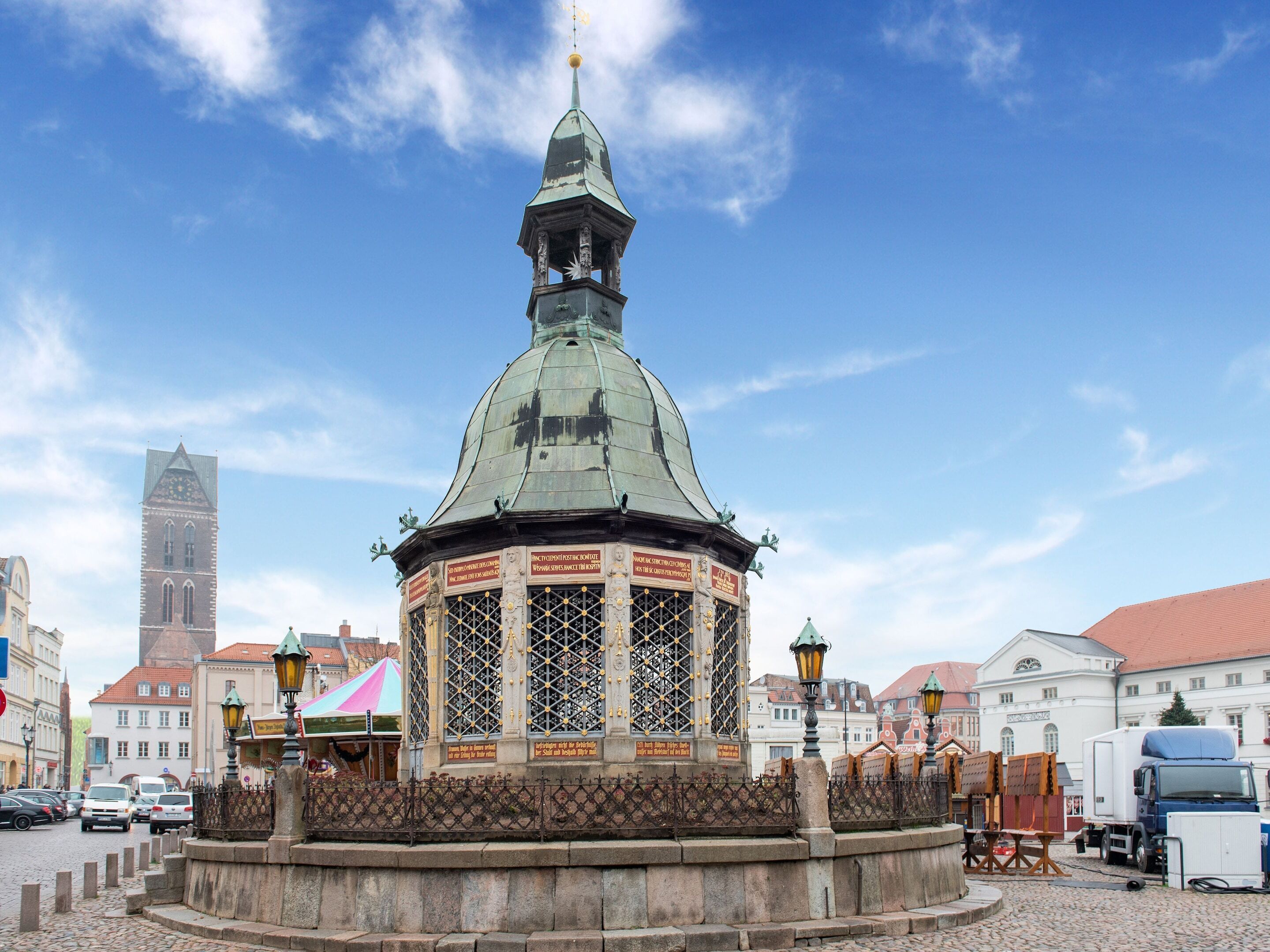 Ein historischer Turm mit einer Uhr, umgeben von Kopfsteinpflasterstraßen und traditioneller Bebauung.