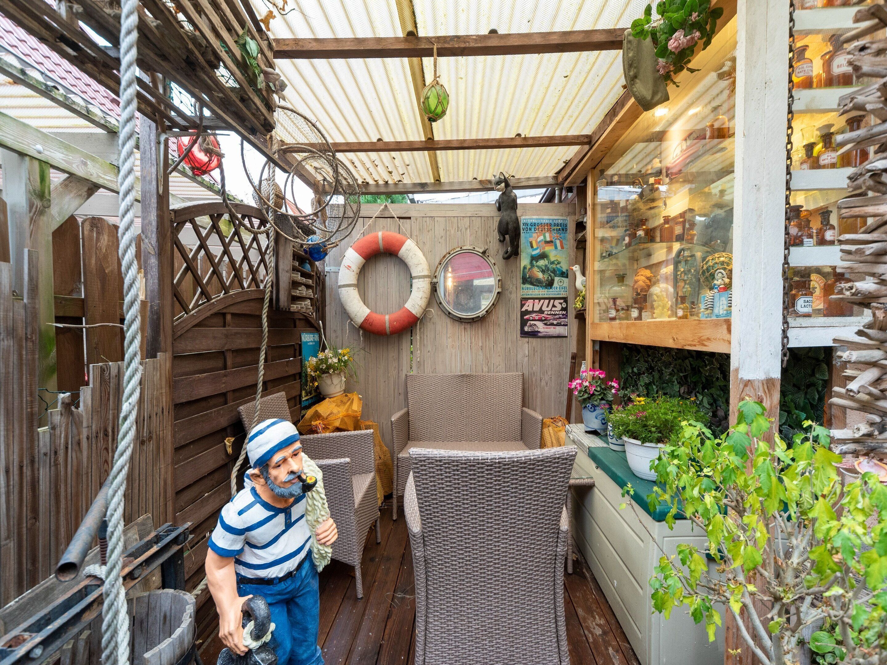 A covered outdoor area with wicker furniture, a wooden fence, and a shop displaying various items.