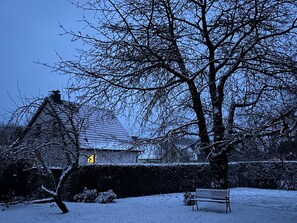 A snow-covered landscape with a bench, a house, and bare trees against a twilight sky. - Gustow Garden Retreat (Gustow)