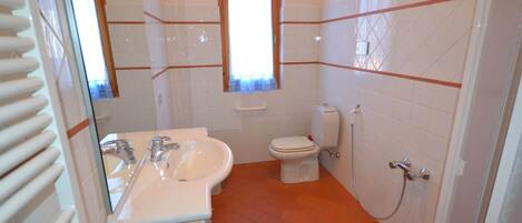 Un baño con un lavamanos blanco, espejo e inodoro. Hay una ventana sobre el inodoro y un radiador a la izquierda.