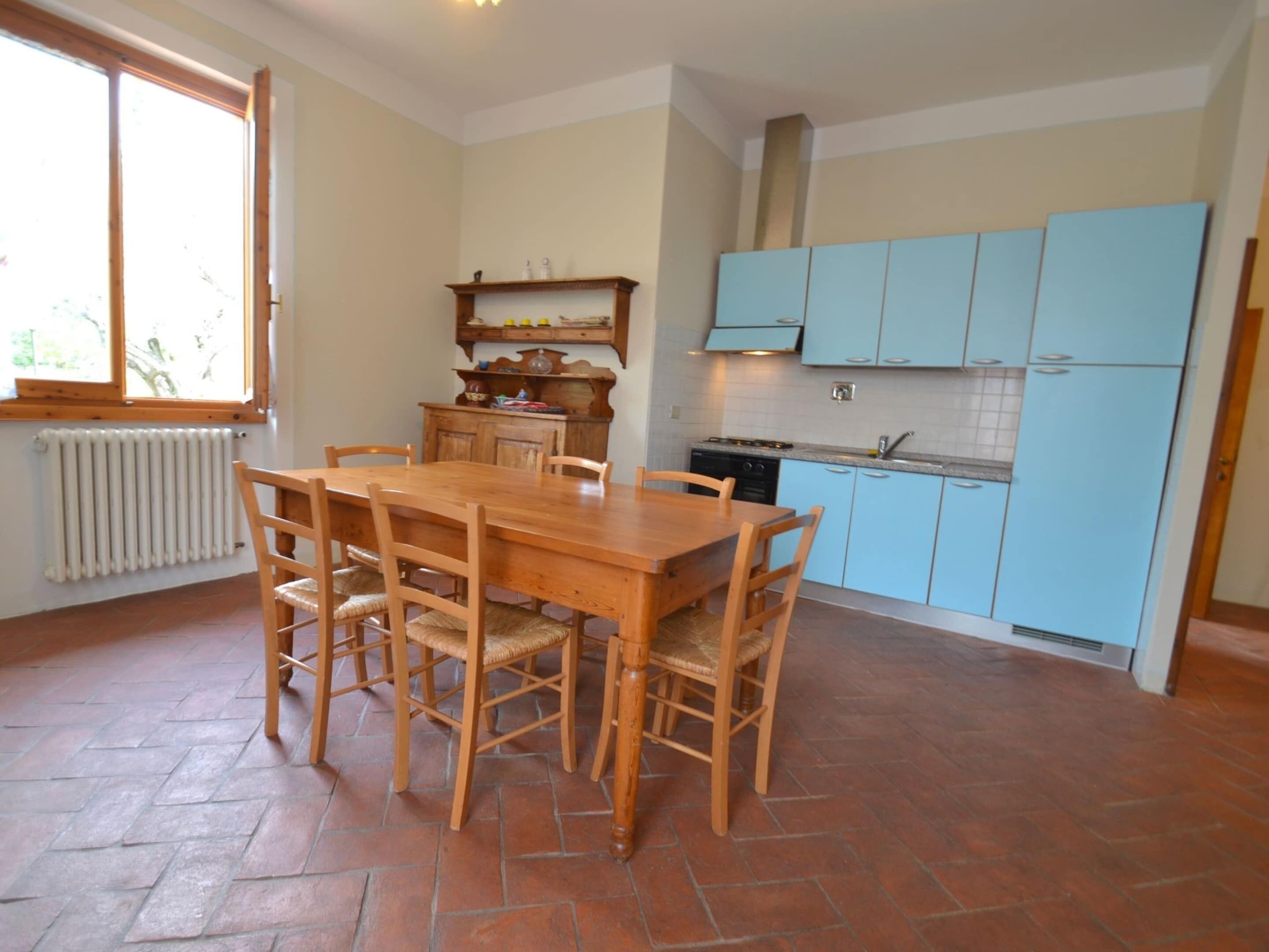 A kitchen with a wooden table and chairs, light blue cabinets, a radiator, and a window.