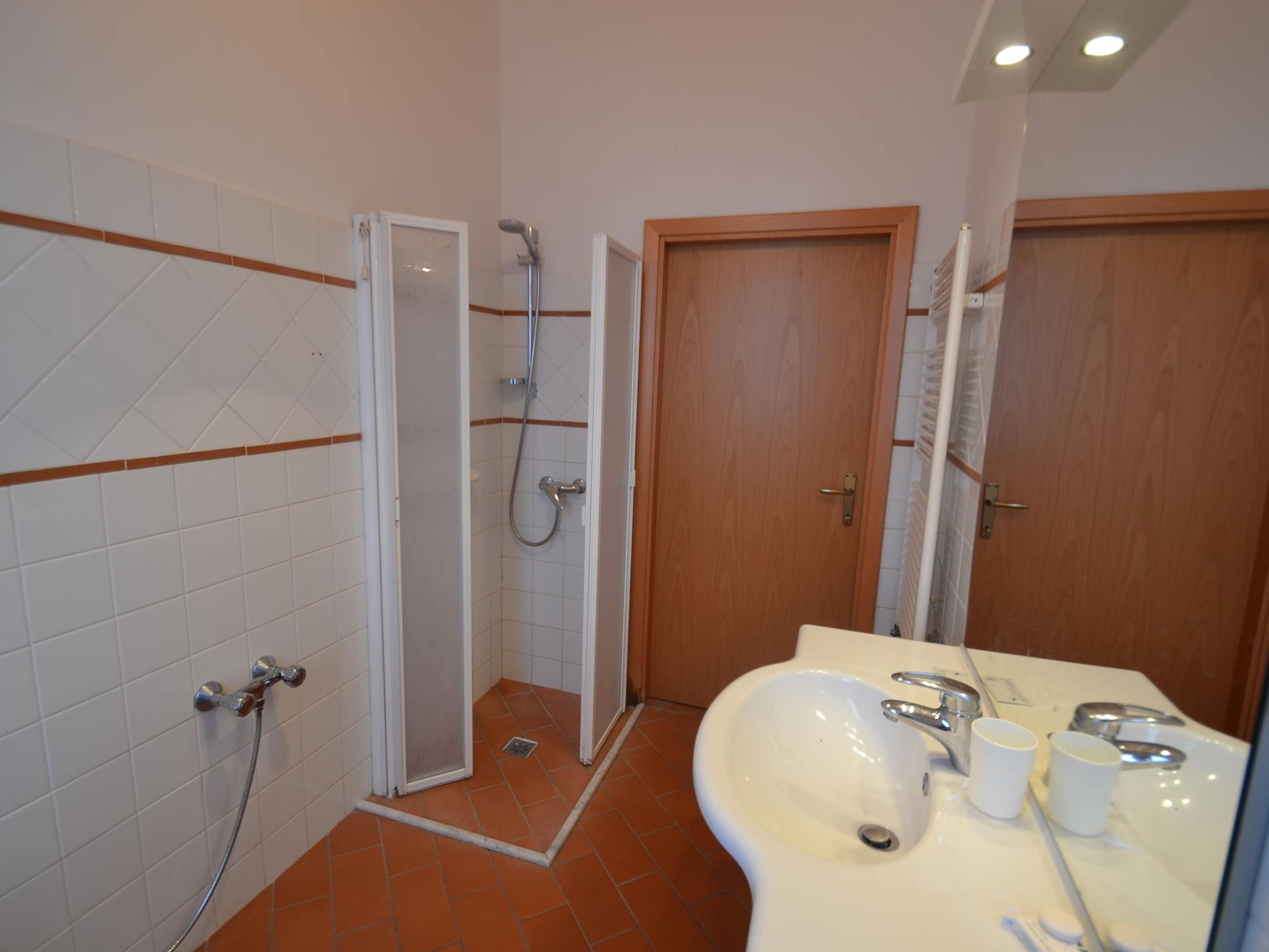 A bathroom with a shower, a sink, and two doors.