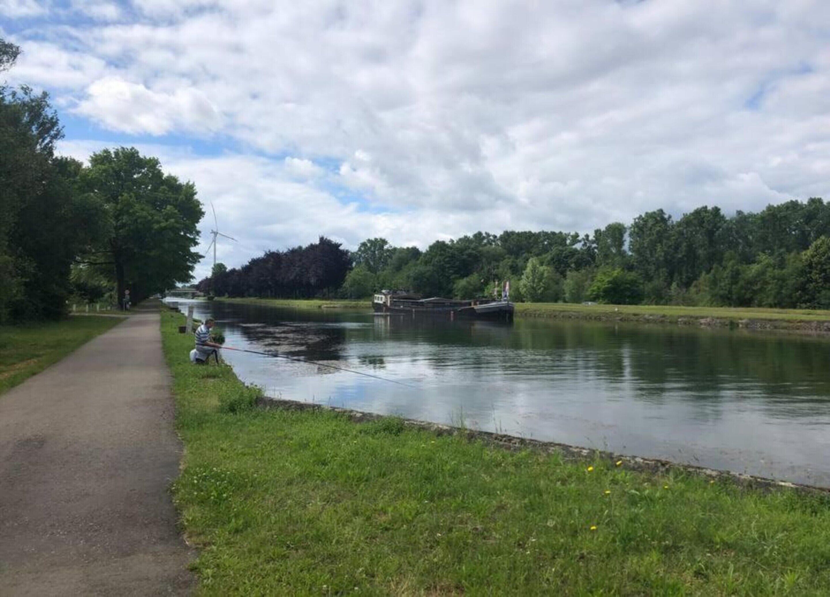 Un étroit canal, bordé d’un sentier, et entouré de verdure et d’arbres.