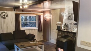 A cozy living room with a sofa, a coffee table, a fireplace, and a window with curtains. - Forest Chalet in Lanklaar (Dilsen-Stokkem)