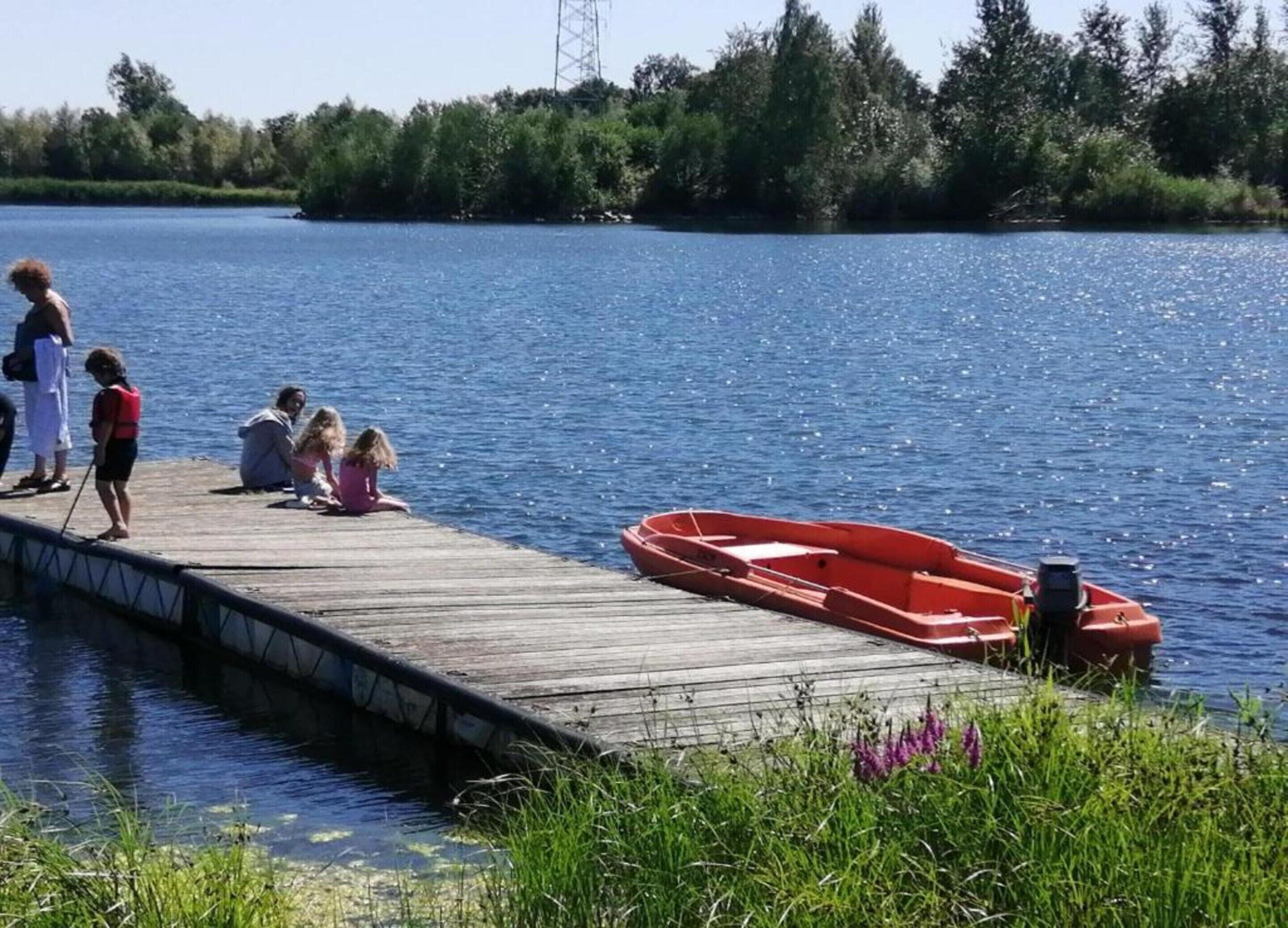 Un muelle de madera que se adentra en un lago tranquilo, con un barco rojo amarrado al final.