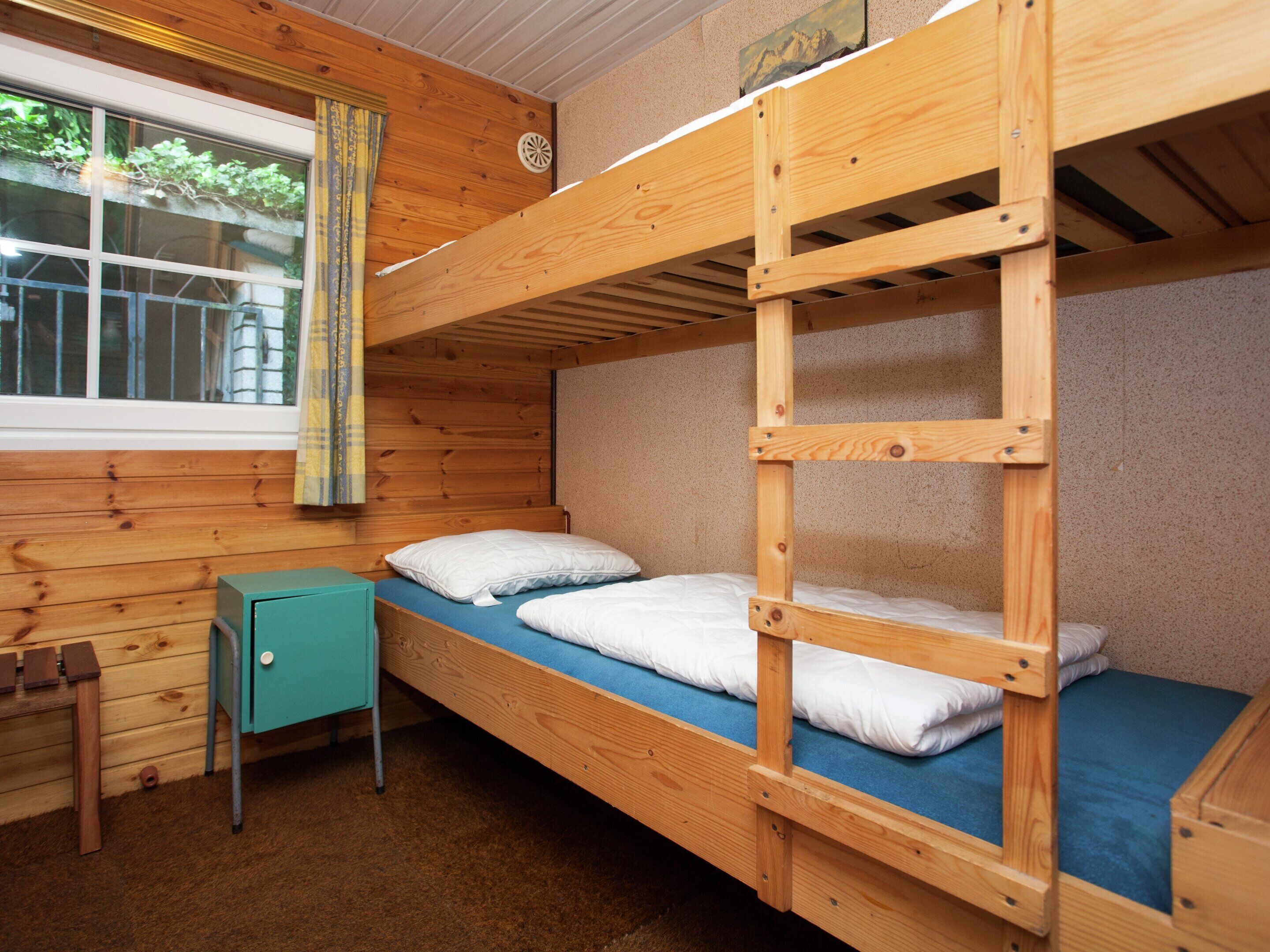 A bunk bed room with a window, a desk, and a small cabinet.
