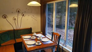 A dining table set with plates, cups, and saucers, a bench, and a window with a view of trees. - Forest Chalet in Lanklaar (Dilsen-Stokkem)