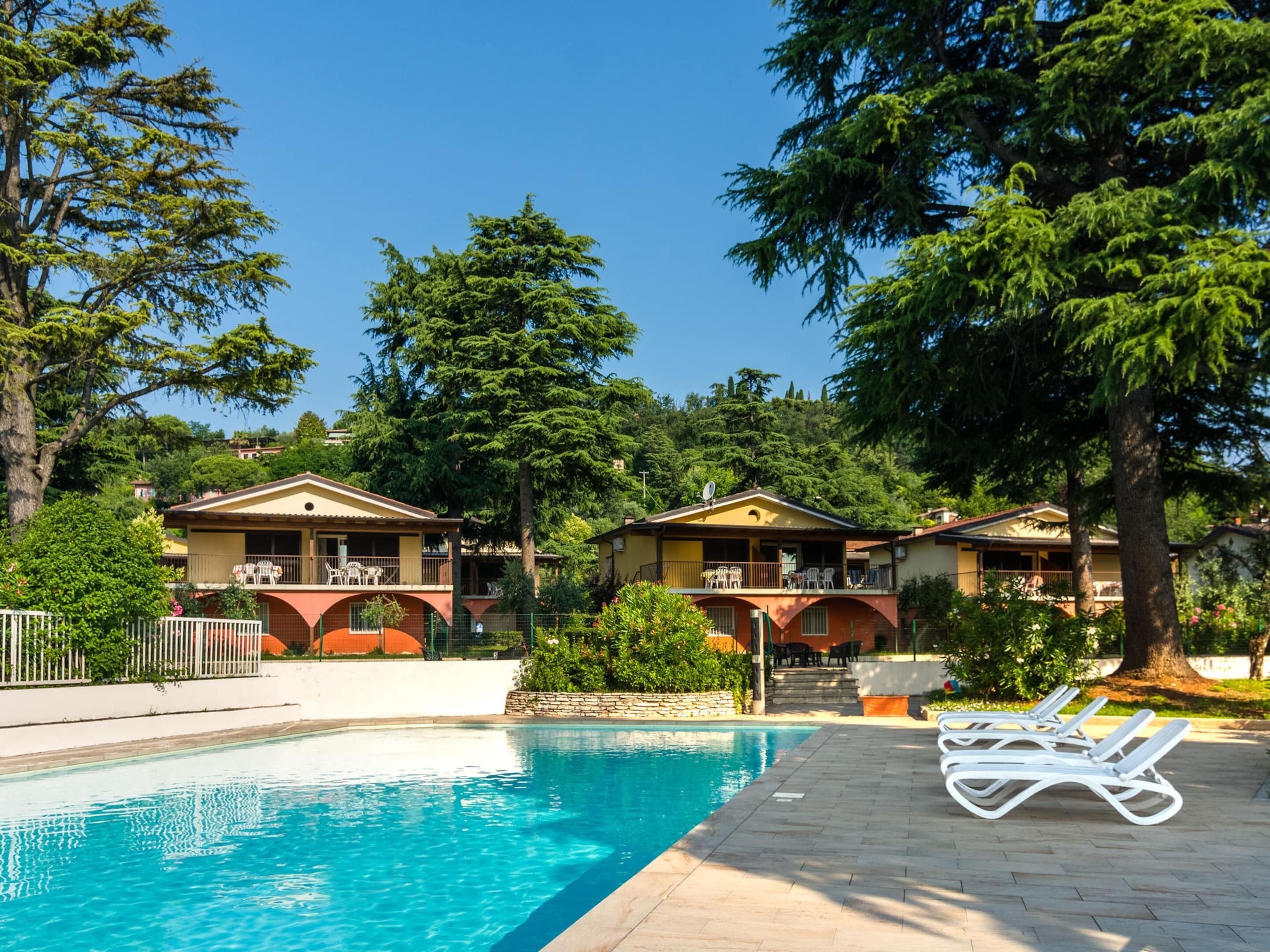 A pool area with lounge chairs, a swimming pool, and two buildings with balconies.