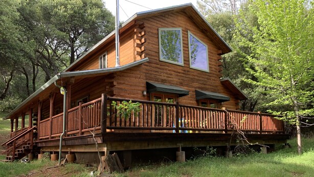A wooden cabin with a balcony, surrounded by trees.