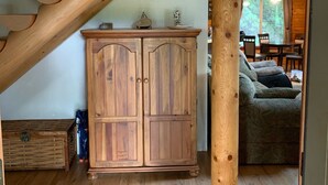 A wooden staircase with a wooden cabinet below it, a wicker chest, and a sofa in the background.