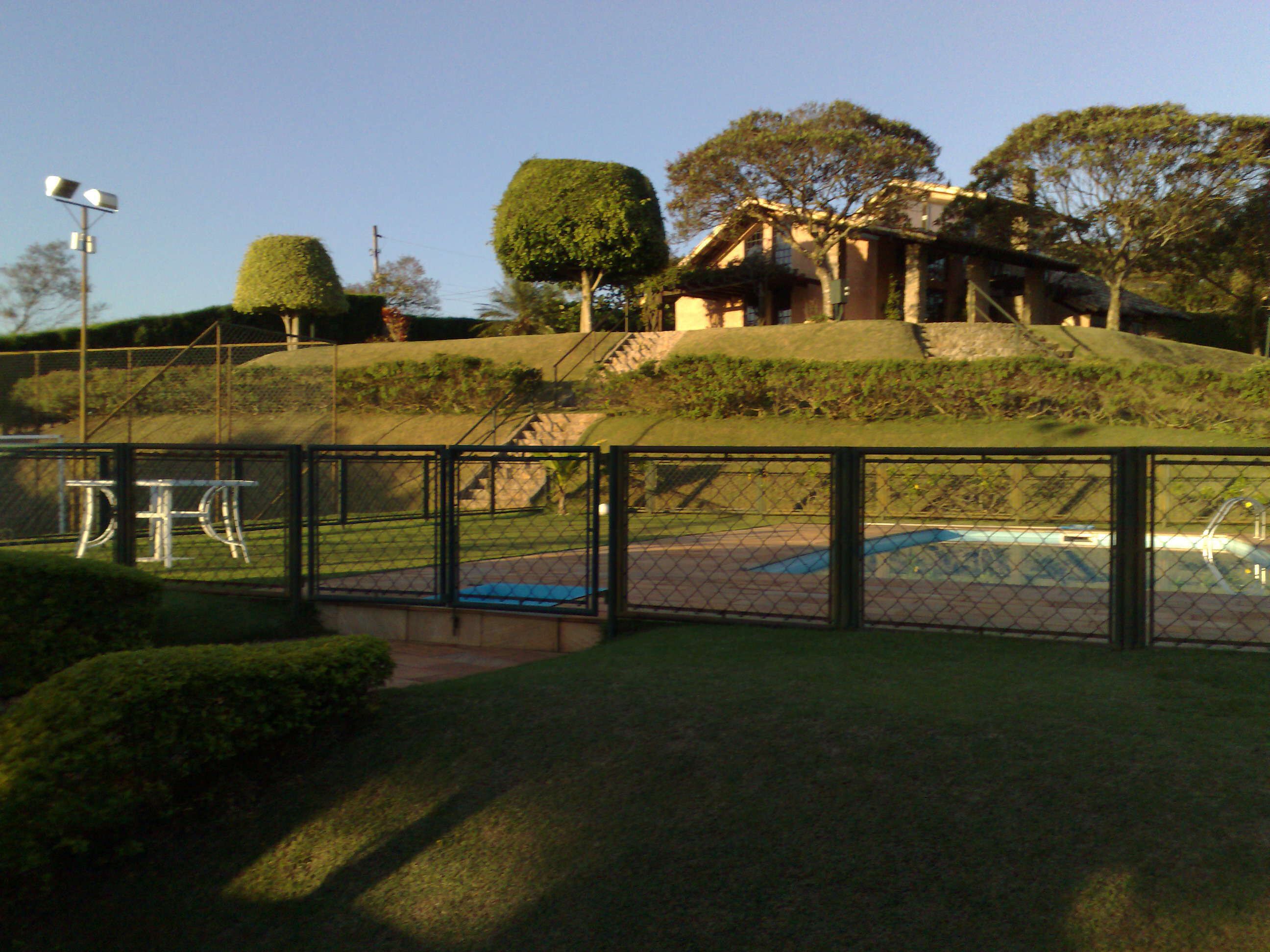 A fenced area with a pool, a house on a hill, and a well-maintained lawn.