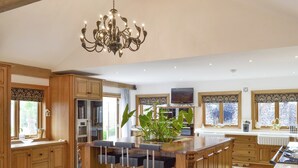 A spacious kitchen with wooden cabinets, a central island with bar stools, a chandelier, and a stone wall view. - 5 bedroom accommodation in Stalmine, near Poulton-le-Flyde (Stalmine, near Poulton-le-Flyde)