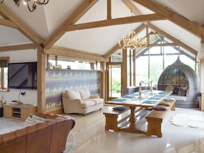 Une pièce spacieuse avec un plafond haut, des poutres en bois, un lustre, une grande fenêtre, un canapé, une table à manger et un coin salon avec des coussins.
