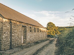 A stone building with a sloped roof, a dirt path leading to it, and a tree-lined landscape in the background. - 3 bedroom accommodation in Abercych, near Cardigan (Abercych, near Cardigan)