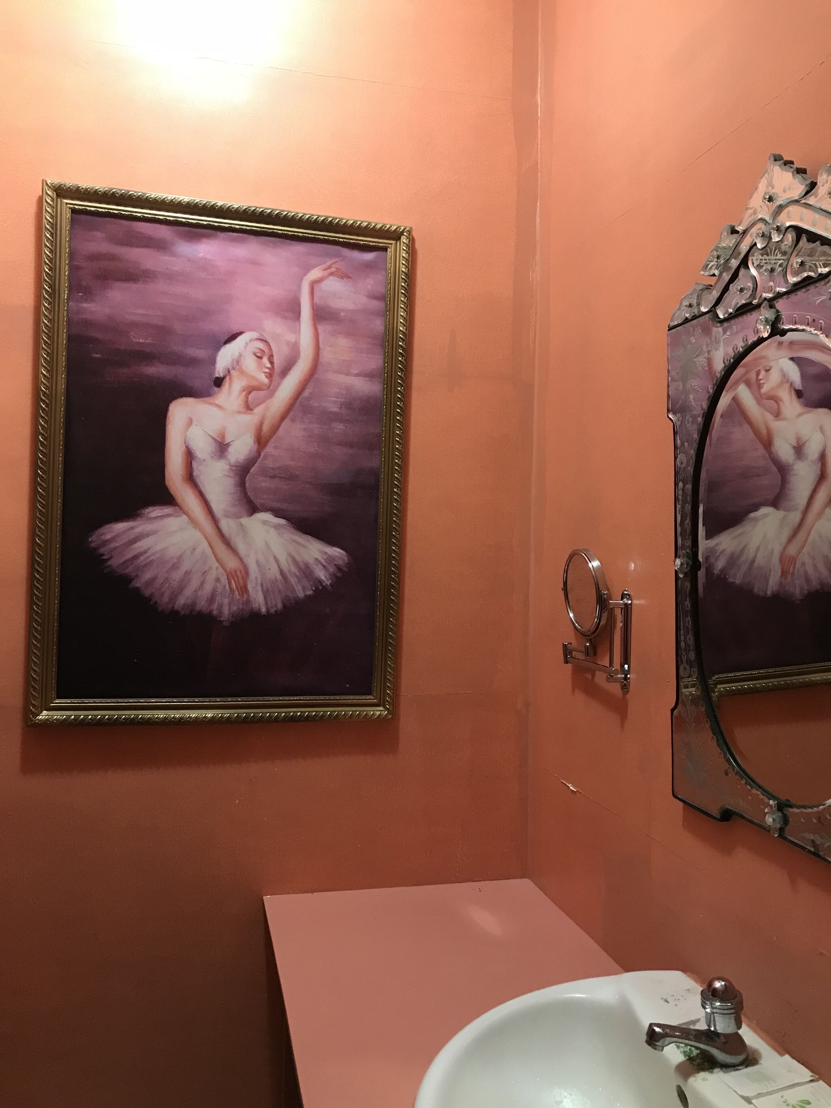 Un baño con un espejo grande, un lavabo y un cuadro enmarco de una bailarina.