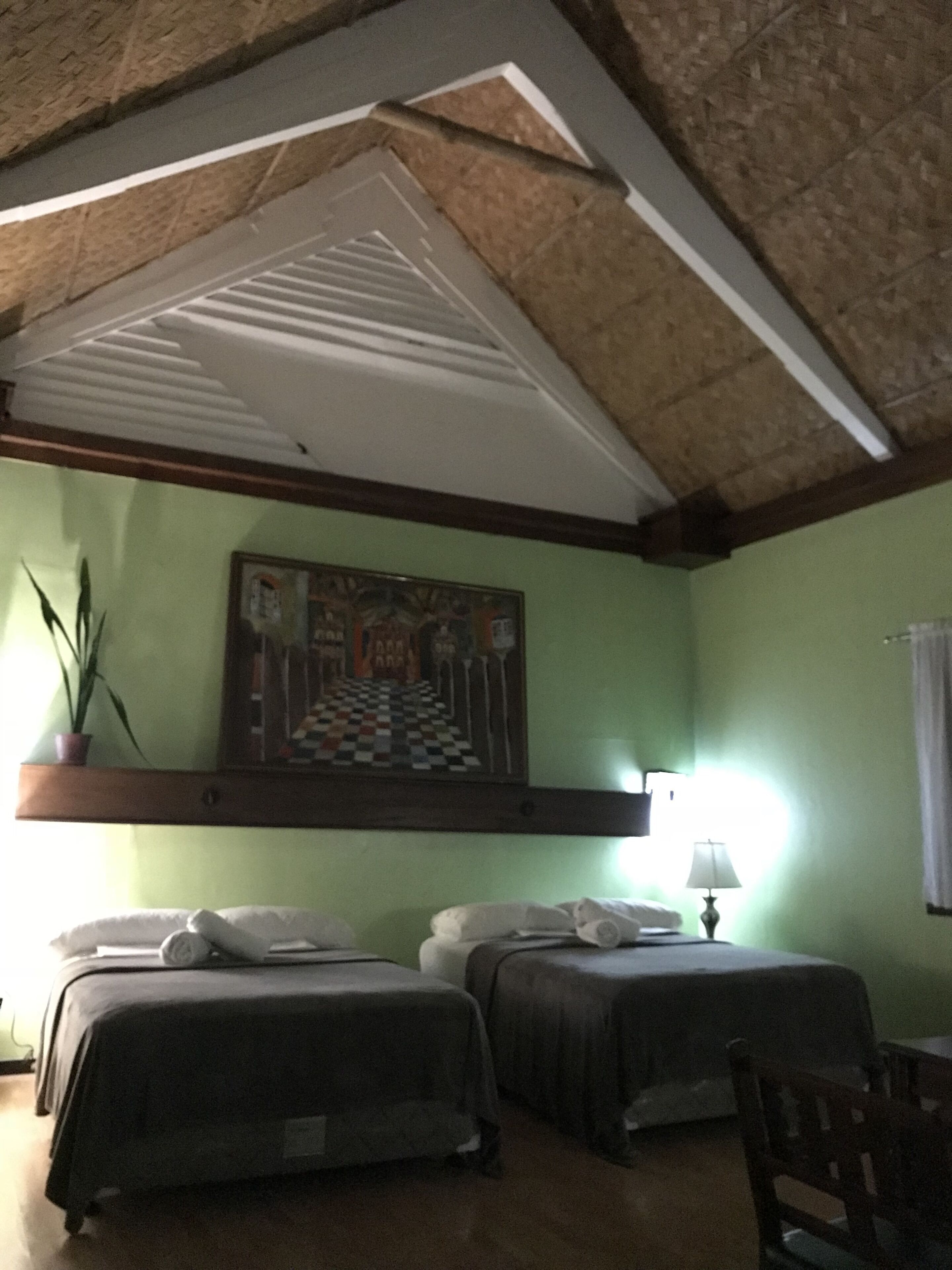 A room with two beds, a painting on the wall, a lamp, and a chair.