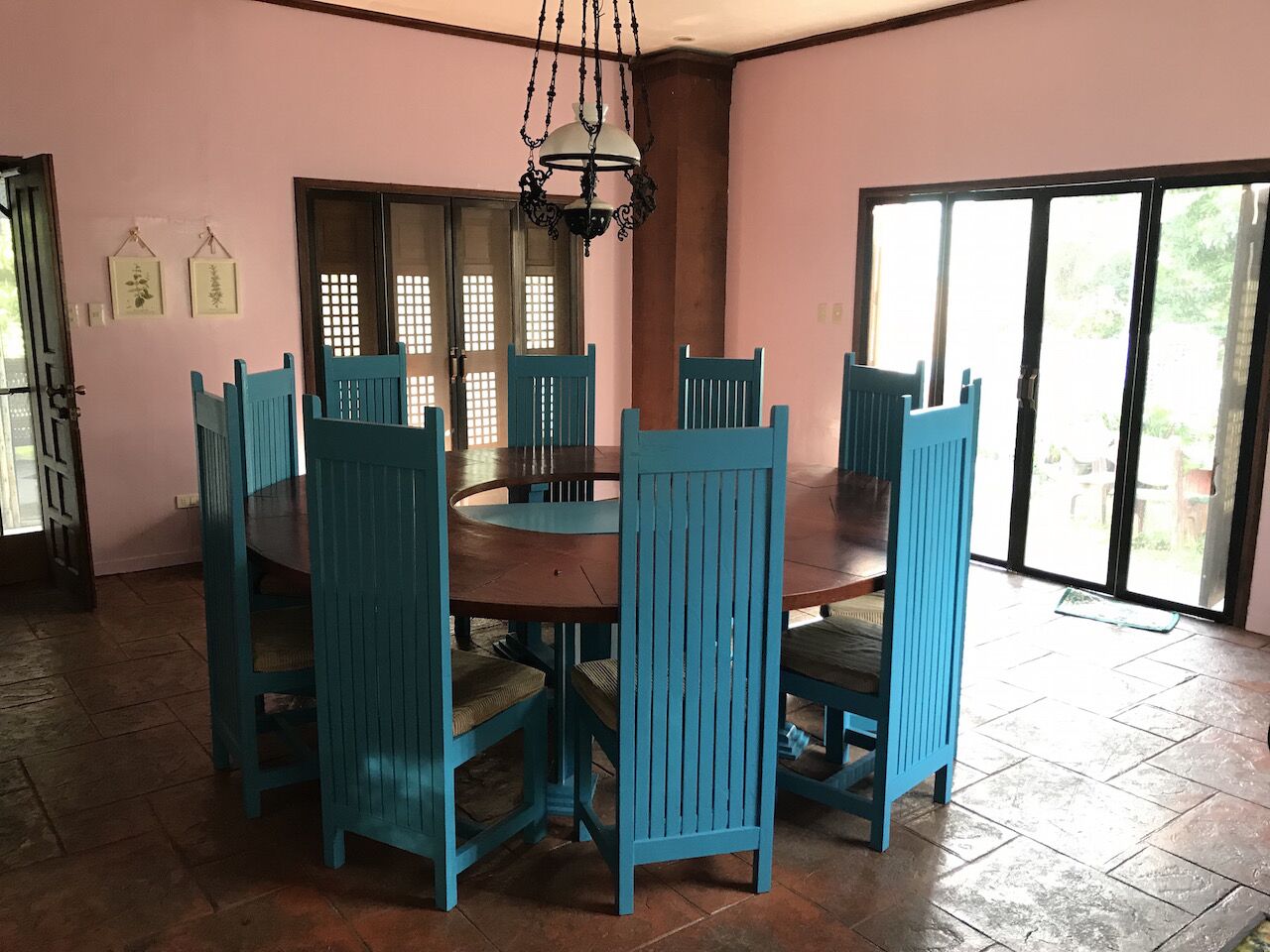 Ein Essbereich mit einem runden Tisch, sechs blauen Stühlen, einer Kristallleuchter und einer Glasschiebetür, die zu einem Außenbereich führt.