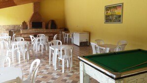A billiards table, white plastic chairs, and a brick fireplace in a room with yellow walls.
