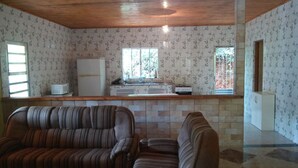 A room with striped sofas, a tiled backsplash, a refrigerator, and a window with a view of greenery.
