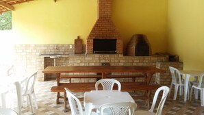 An outdoor patio with a brick fireplace, a wooden table, and white plastic chairs.