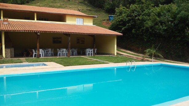 A swimming pool with a clear blue water surface, surrounded by a grassy area and a building with a tiled roof.