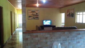 A living room with a tiled floor, a television, a sofa, and a painting on the wall.
