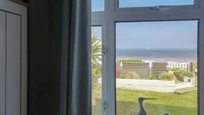 A room with a large window overlooking a beach and a grassy area with two birds. - 2 bedroom accommodation in East Runton, near Cromer (East Runton, near Cromer)