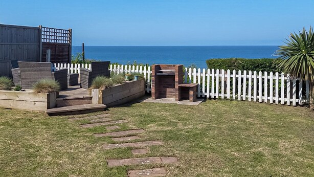 A backyard with a white picket fence, a brick barbecue area, and a view of the sea. - 2 bedroom accommodation in East Runton, near Cromer (East Runton, near Cromer)
