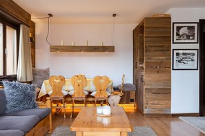 A cozy living room with a wooden sofa, a wooden dining table, and a bench with heart-shaped cutouts. - App Les Rocailles 9 | family retreat | with Sauna (Riddes)