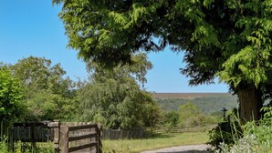 A paved pathway leading to a wooden gate, surrounded by lush greenery and trees. - 4 bedroom accommodation in Goathland (Goathland)