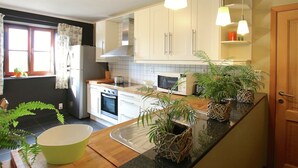 Eine moderne Küche mit weißen Schränken, einer Mikrowelle, einem Backofen und einem Spülbecken. Auf der Arbeitsfläche stehen Blumentöpfe und es gibt ein Fenster mit Vorhängen.