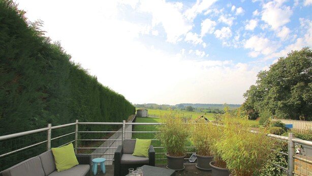 Eine Terrasse mit Gartenmöbeln, Topfpflanzen und Blick ins Grüne.