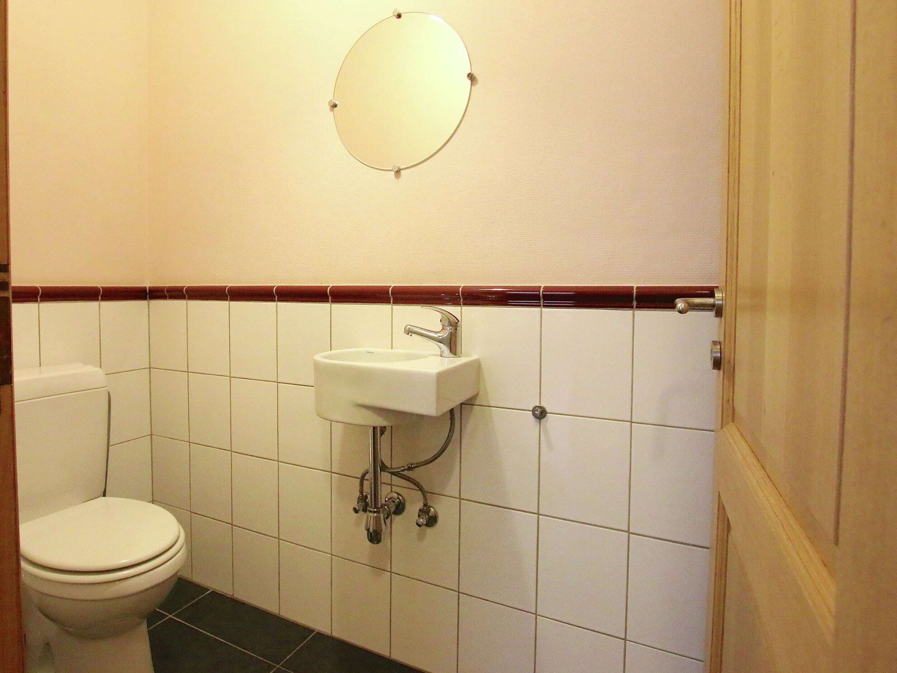 Et lille, rent badeværelse med toilet, vask og spejl.
