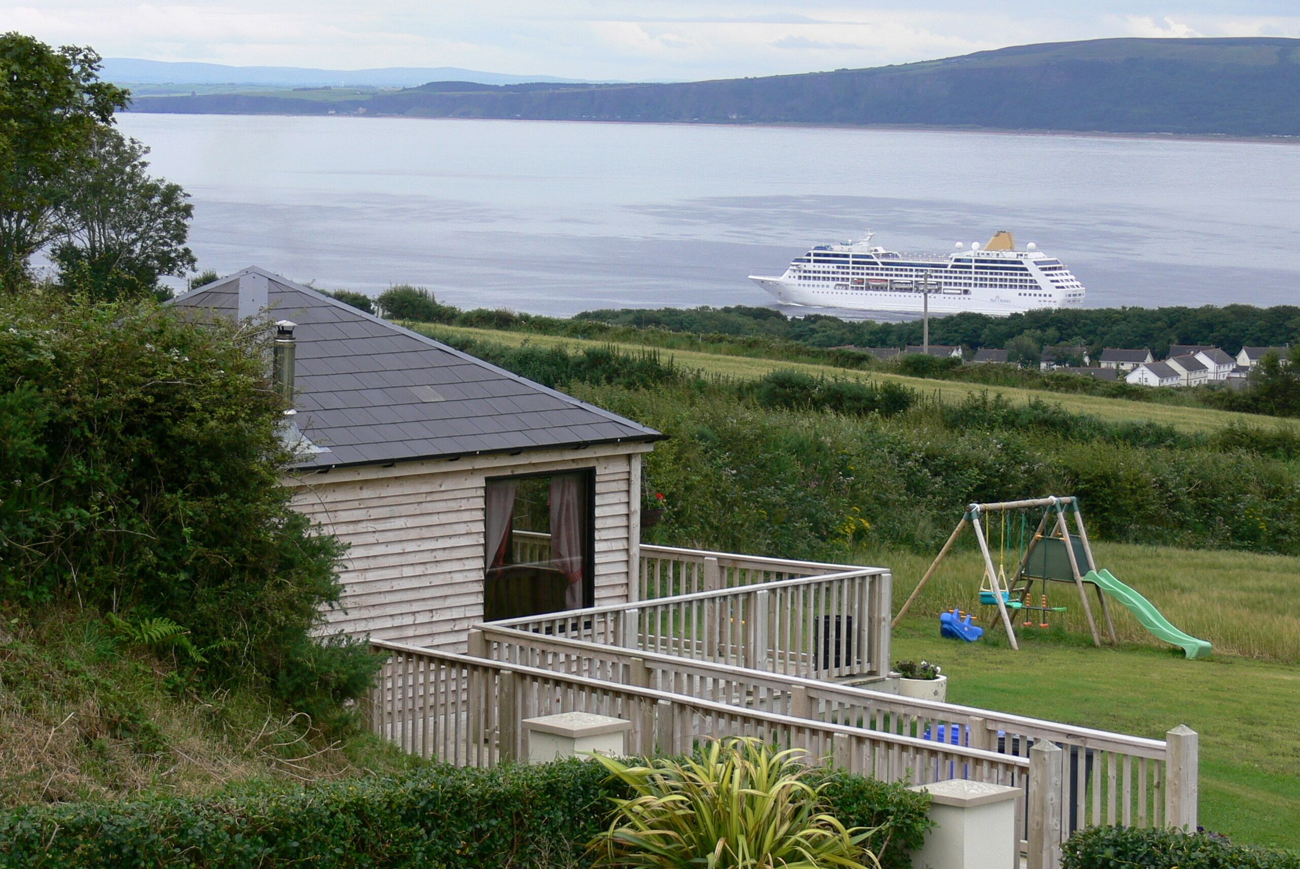 A house with a deck overlooking a body of water and a cruise ship in the distance.