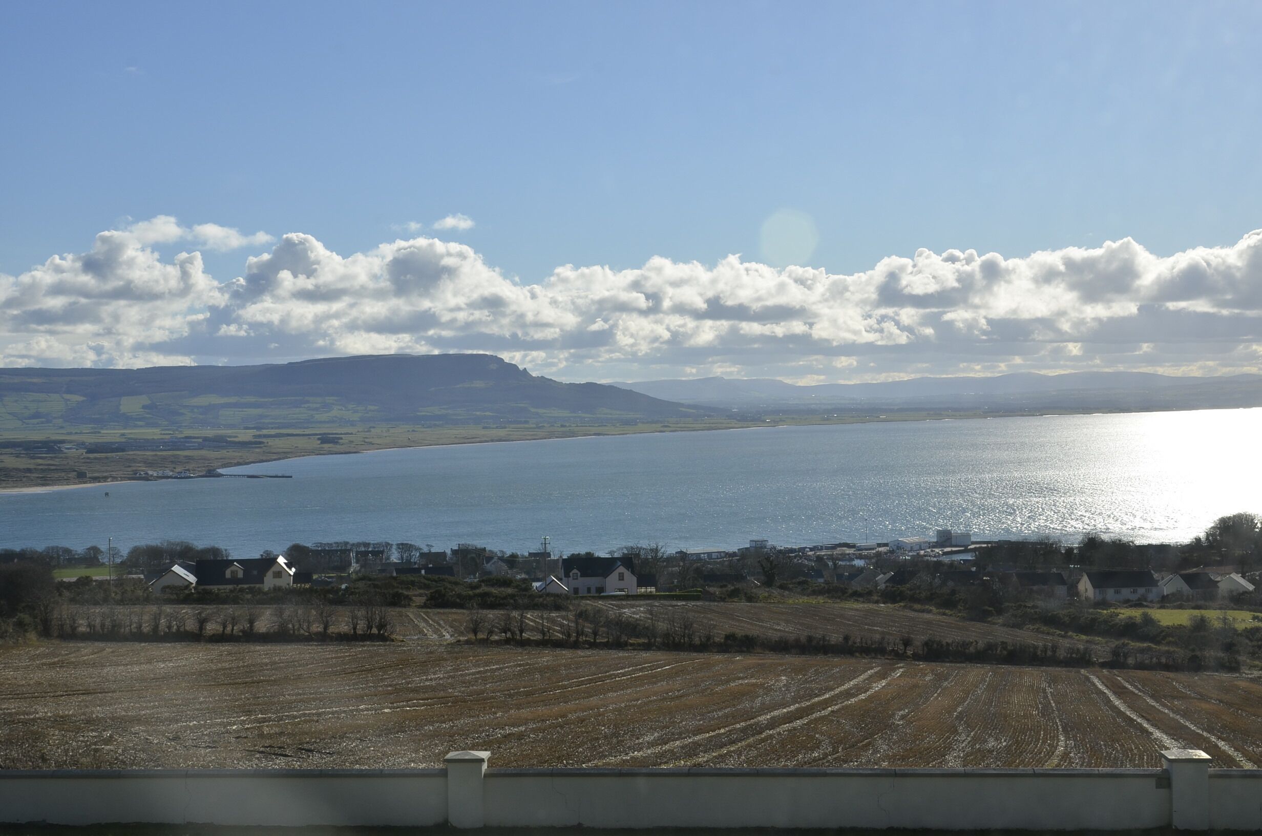 A coastal landscape with a body of water, fields, and scattered houses.