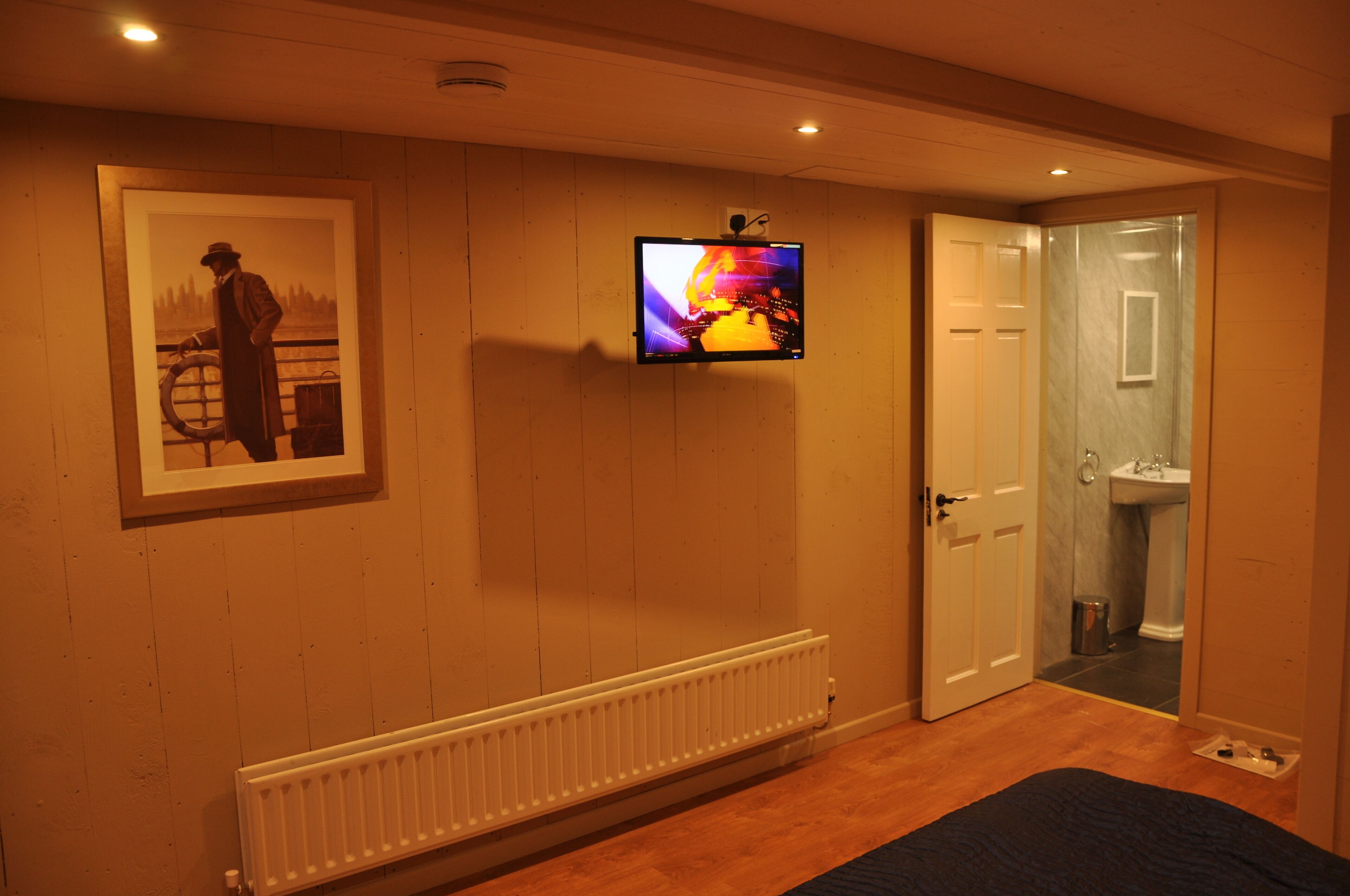 A room with a bed, a radiator, a television mounted on the wall, and a door leading to a bathroom.
