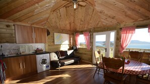 A wooden cabin interior with a kitchen, a sofa, a dining table with chairs, and a view of the outdoors. - RUSTIC LOG CABIN LOCATED GREENCASTLE CO DONEGAL (Greencastle)